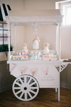 a white cart filled with cakes and cupcakes on top of a wooden floor