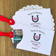 two white envelopes with red ribbon on top of a wooden table next to lace doily