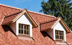 two windows on the roof of a house with red tile and shingles, against a blue sky