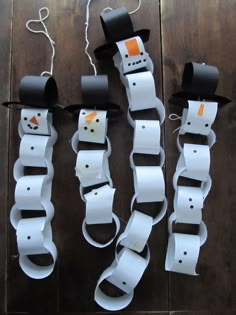 three snowmen made out of toilet paper on top of a wooden table with string attached to them