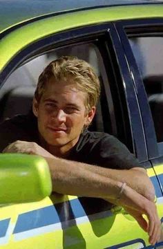 a young man sitting in the drivers seat of a green car looking out the window