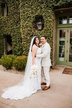 a bride and groom standing in front of a building with ivy on the wall behind them