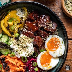 a bowl filled with meat and vegetables on top of a wooden table next to a fork