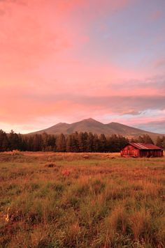 a red barn in the middle of a field with mountains in the background at sunset