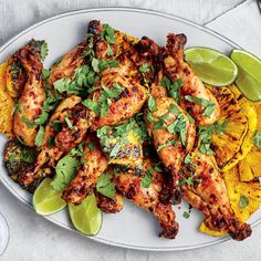 a white plate topped with chicken and tortillas next to lime wedges on a table