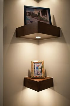 two wooden shelves with pictures on them in a corner next to a framed photograph and light fixture