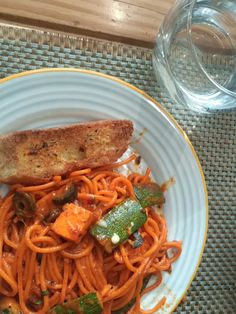 a white plate topped with pasta and meat next to a glass of water on top of a table