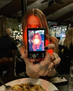 a woman taking a selfie with her cell phone at a dinner table in a restaurant