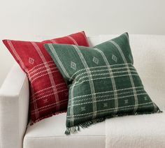 two red and green pillows sitting on top of a white couch next to each other