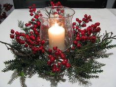 a candle that is sitting on a table with some red berries and greenery around it