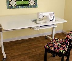 a sewing machine sitting on top of a white table next to a quilted wall hanging