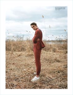 a man standing in a field with his hands on his hips wearing a red suit and white sneakers