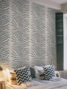 a bedroom with zebra print wallpaper and pillows on the bed, next to a window