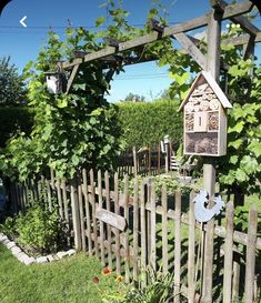 a bird house is hanging on a wooden trellis in the grass near a fence