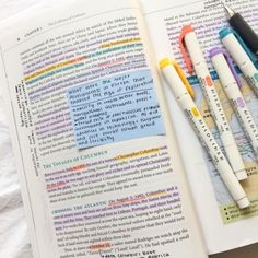 an open book with four pens on top of it next to some writing and markers