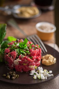 a black plate topped with meat and veggies on top of a wooden table