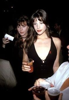 a woman in a black dress standing next to other people at a party with drinks