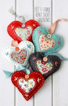 four heart shaped ornaments hanging on a white wooden wall with ribbons and buttons attached to them