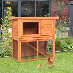 an orange chicken coop with two chickens in the grass next to it and a brick building behind it