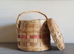 a woven basket with lid sitting on top of a gray table next to a white wall