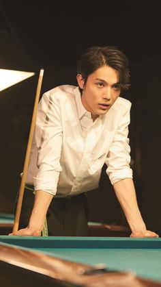 a man leaning over a pool table with a cue in his hand and looking at the camera