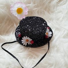 a black hat with flowers on it sitting on a white fur covered floor next to a pink flower