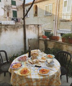 an outdoor table with food on it in front of a building and some people eating outside