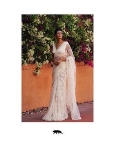 a woman in a white sari standing next to a wall with flowers on it