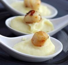 three white spoons filled with food on top of a black plate and topped with scallops