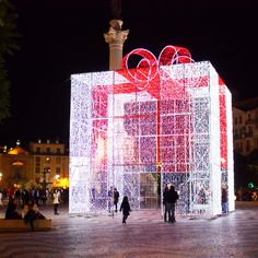 people are standing in front of a large box with presents on it at night time