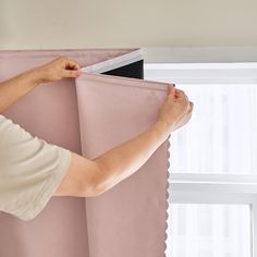 a woman is opening the curtain with her hands and pulling it up against the wall