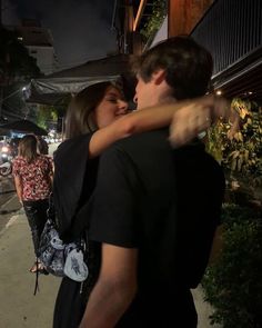 a man and woman embracing each other on the sidewalk in front of a building at night