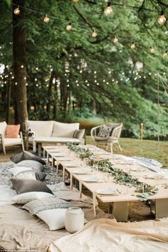 a long table set up with place settings for dinner in the middle of a forest