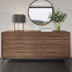 a modern dresser with a round mirror above it and a lamp on the sideboard