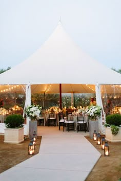 a large white tent set up with tables and chairs for an outdoor wedding reception in the evening