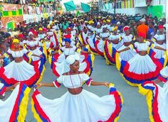 a group of women in colorful dresses dancing on the street with people watching from behind