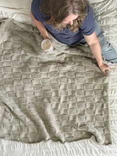 a woman laying on top of a bed next to a blanket and coffee mugs