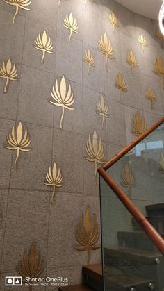 the wall has gold leaves on it and is next to a stair case with glass railings