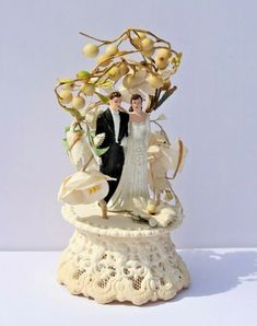 a bride and groom figurine sitting on top of a white pedestal with flowers