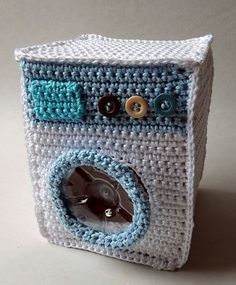 a crocheted white and blue box with buttons on the front is sitting on a table