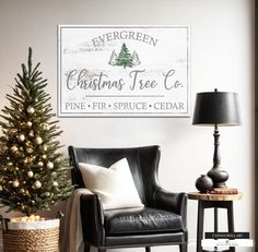 a christmas tree sitting next to a black chair in a living room with a white sign on the wall