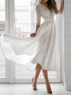 a woman in a white dress is standing by a window