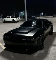 a black muscle car parked in a parking lot at night with other cars behind it