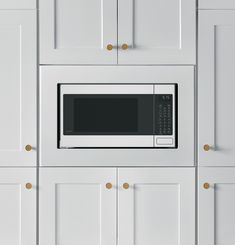 a microwave built into the side of a white kitchen cabinet with gold knobs on it