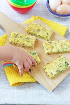 a child reaching for food on a cutting board with eggs and other ingredients around it