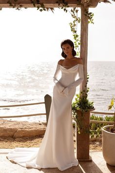 a woman in a white wedding dress standing under a pergolated structure near the ocean