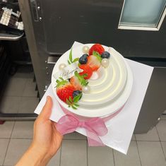 a person holding a cake with strawberries and blueberries on top