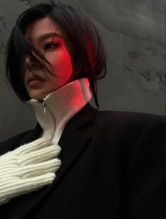 a woman with black hair wearing a white sweater and red light under her collar is looking at the camera