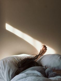 a woman laying on top of a white bed under a light shining through the window