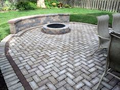 an outdoor fire pit surrounded by brick pavers and chairs in a backyard with grass